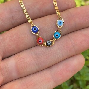 May include: A gold chain necklace with five evil eye charms. The charms are blue, blue, black, red, and blue. The chain is a curb chain style.