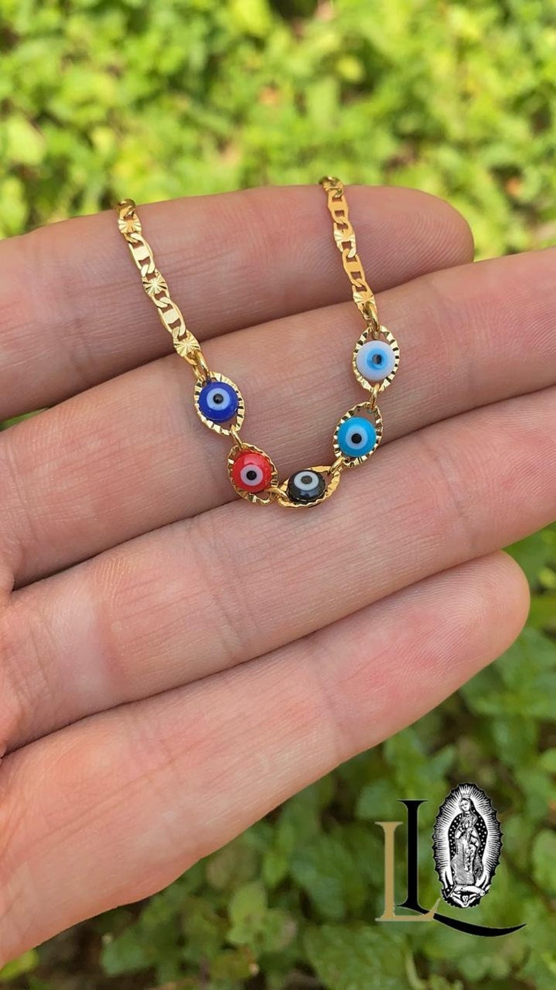 May include: A gold chain necklace with five evil eye charms. The charms are blue, blue, black, red, and blue. The chain is a curb chain style.