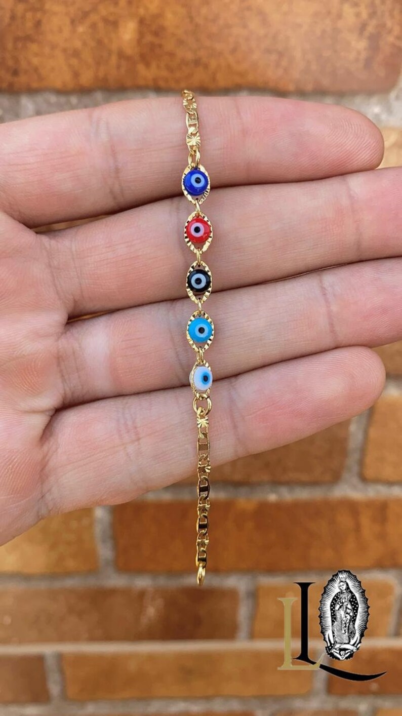May include: Gold chain bracelet with five evil eye charms. The charms are blue, red, black, light blue, and white.