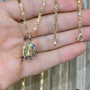 May include: A gold chain necklace with a pendant featuring a depiction of the Virgin Mary. The chain is a box chain with a diamond-cut finish. The pendant is oval-shaped and has a detailed design.