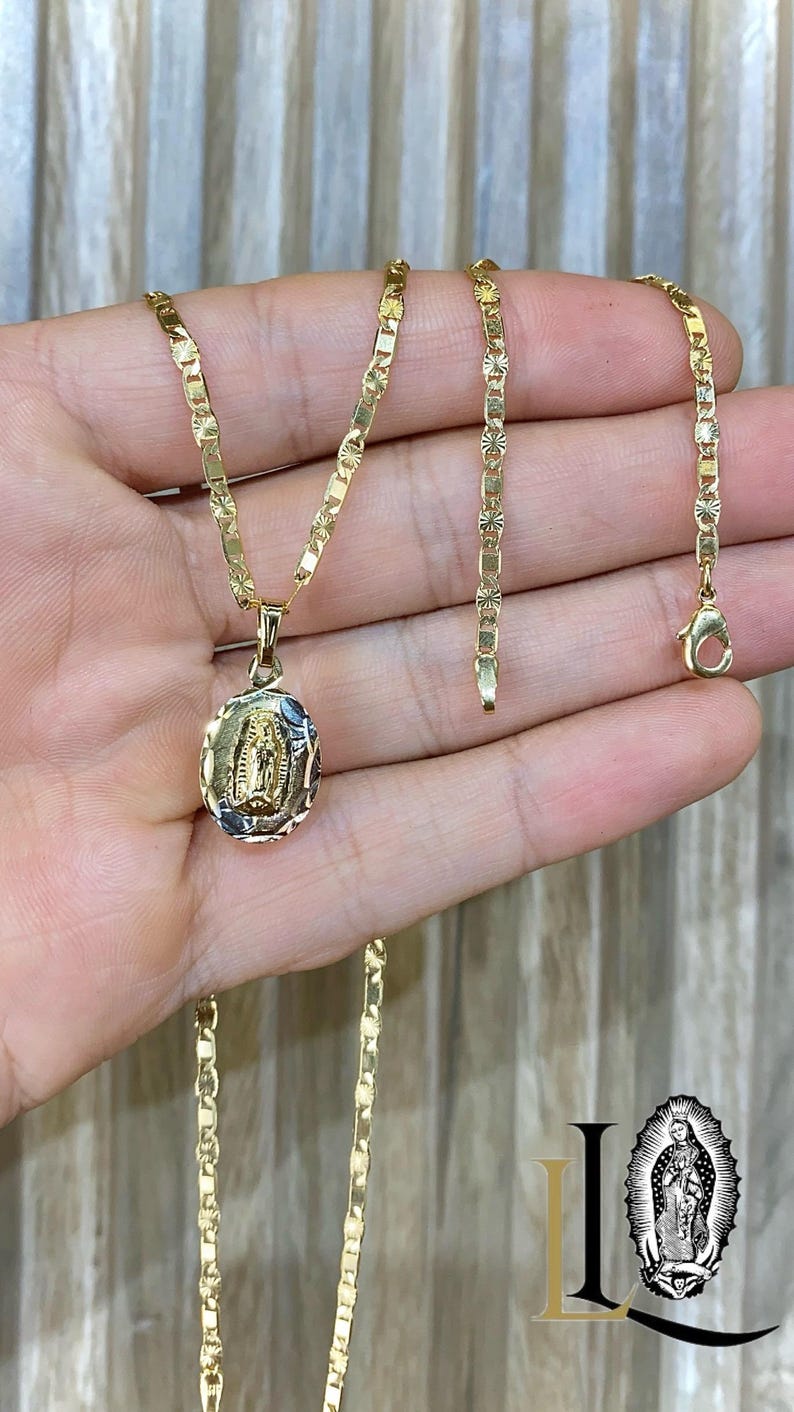 May include: A gold chain necklace with a pendant featuring a depiction of the Virgin Mary. The chain is a box chain with a diamond-cut finish. The pendant is oval-shaped and has a detailed design.