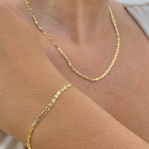 May include: A gold chain necklace and bracelet with a delicate, patterned design. The necklace is worn around the neck and the bracelet is worn on the wrist.
