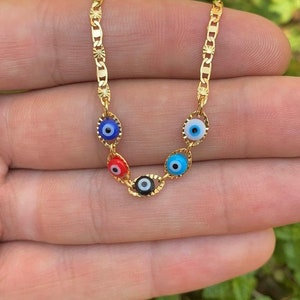 May include: Gold chain necklace with five evil eye charms. The charms are blue, red, black, and white.