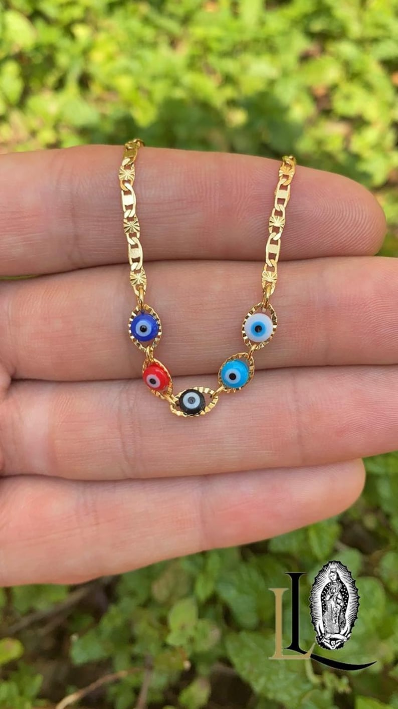 May include: Gold chain necklace with five evil eye charms. The charms are blue, red, black, and white.