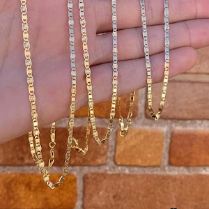 May include: Five gold chains of varying lengths, each with a delicate, patterned design. The chains are displayed on a hand against a brick background.