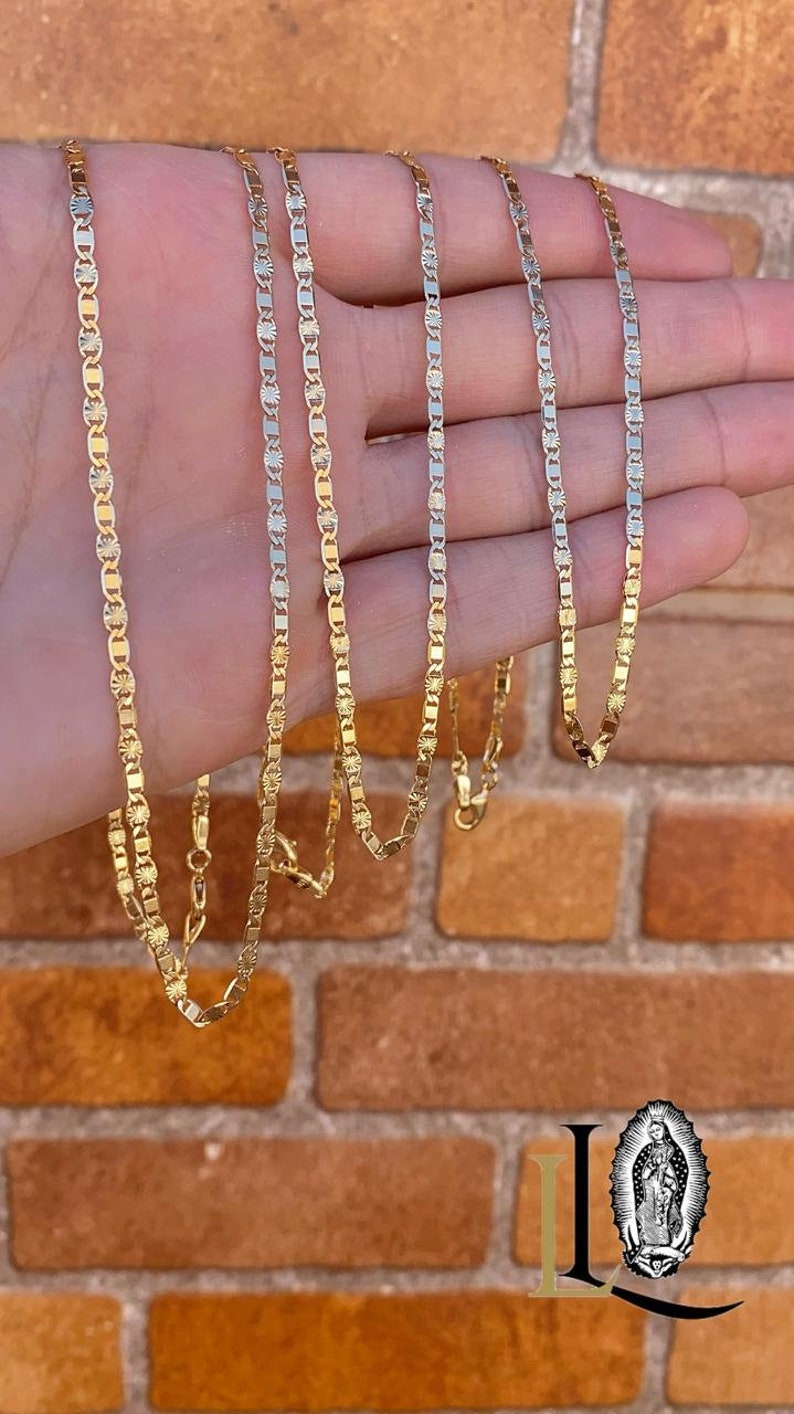May include: Five gold chains of varying lengths, each with a delicate, patterned design. The chains are displayed on a hand against a brick background.