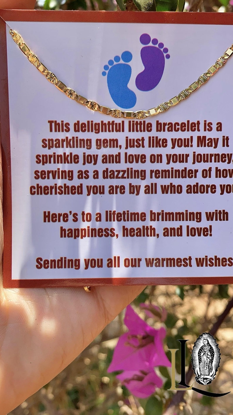 May include: A gold chain bracelet with a delicate design. The bracelet is displayed on a card with a message about joy, love, and happiness. The card also features a pair of blue footprints.