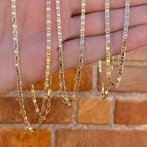 May include: Four gold chains with a diamond-shaped pattern on a hand. The chains are different lengths and are all made of gold.