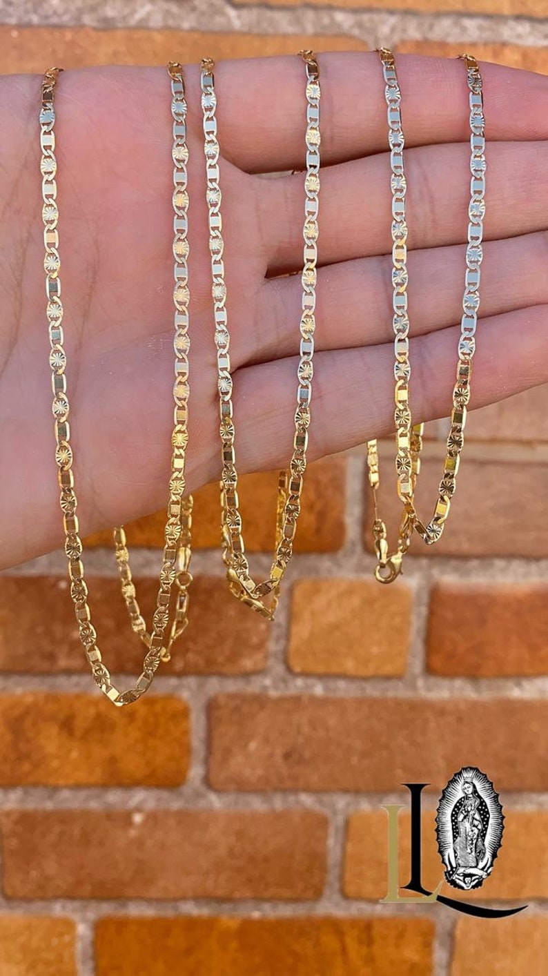 May include: Four gold chains with a diamond-shaped pattern on a hand. The chains are different lengths and are all made of gold.