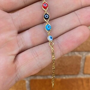 May include: Gold chain bracelet with multiple blue, red, and black evil eye charms.