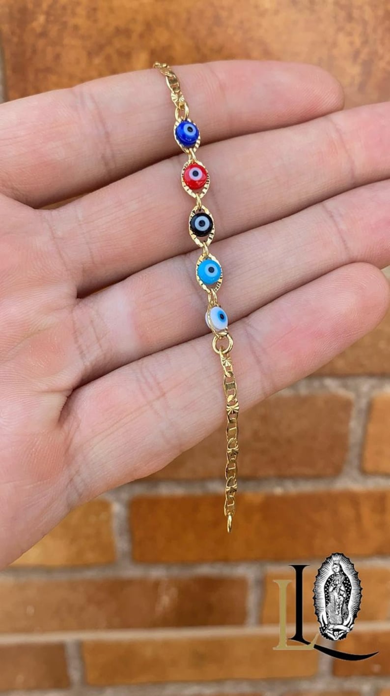 May include: Gold chain bracelet with multiple blue, red, and black evil eye charms.