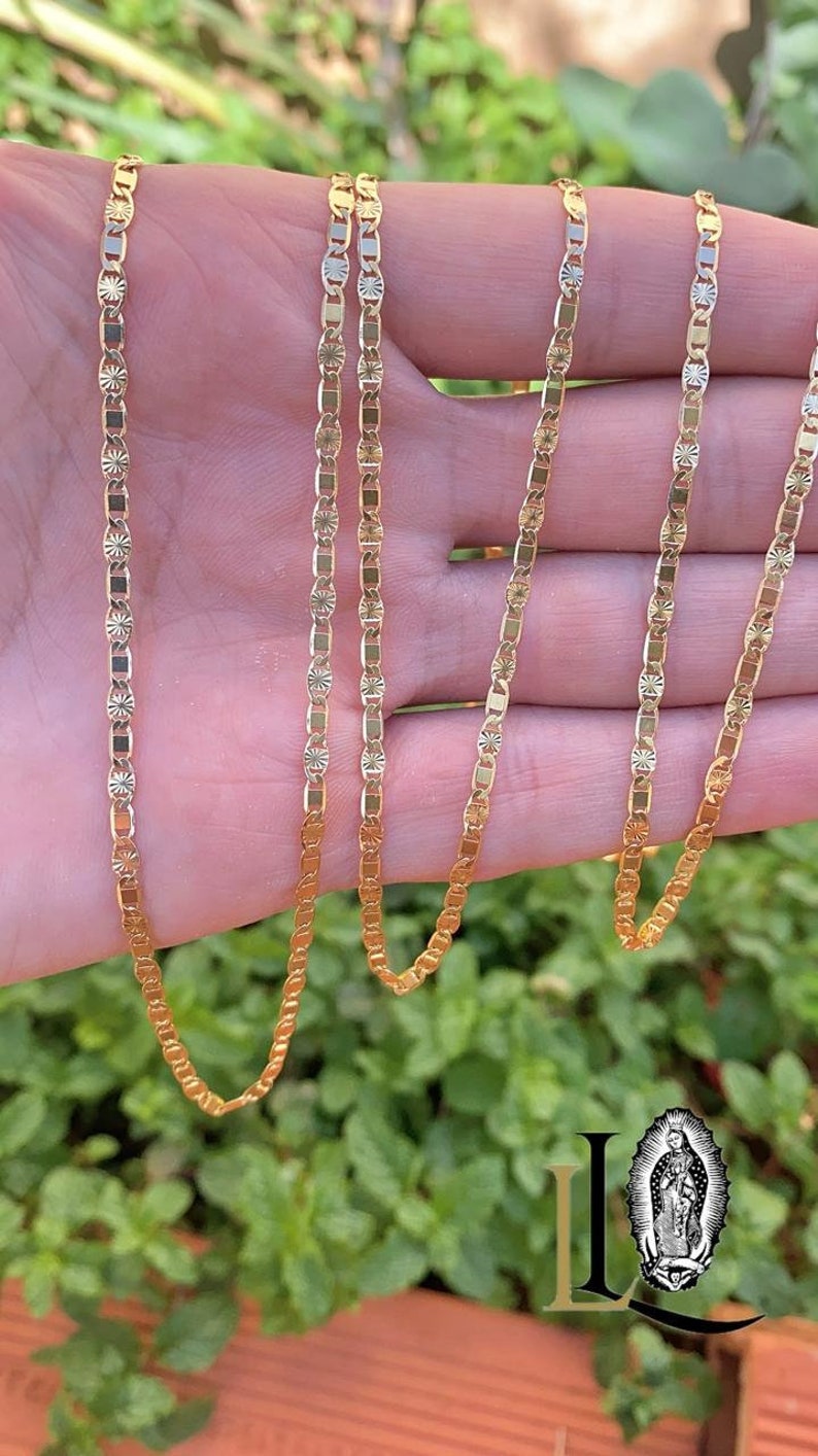 May include: A gold chain necklace with a delicate, patterned design. The chain is made of multiple strands and is shown draped over a hand.