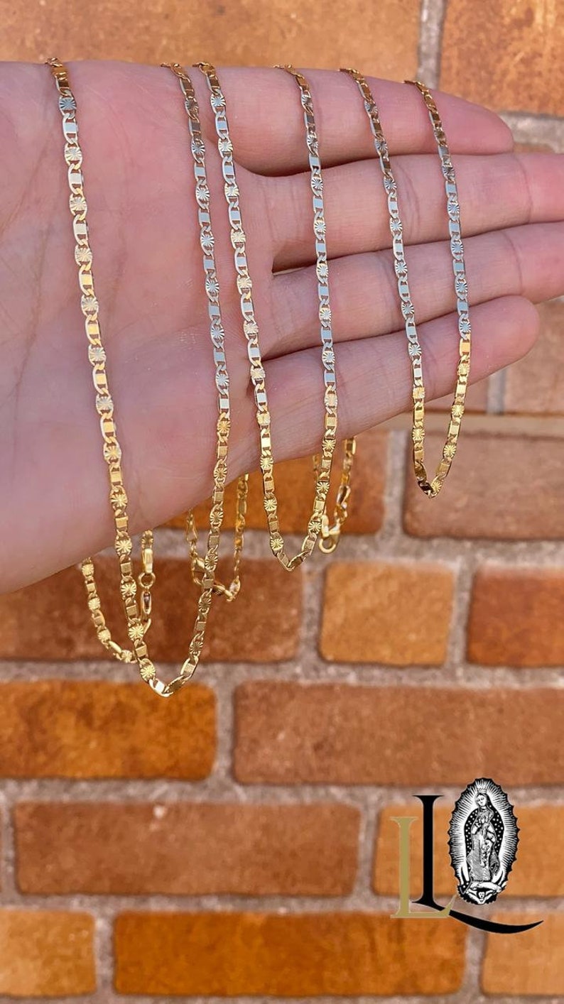 May include: Five gold chains of different lengths, with a textured, diamond-like pattern. The chains are displayed on a hand against a brick wall background.