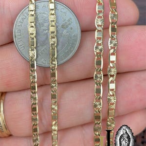 May include: Close-up of several gold-colored chain necklaces with intricate geometric designs. A US quarter coin is placed in the center for size comparison. The chains have a bright, reflective finish, suggesting they are made of a precious metal.