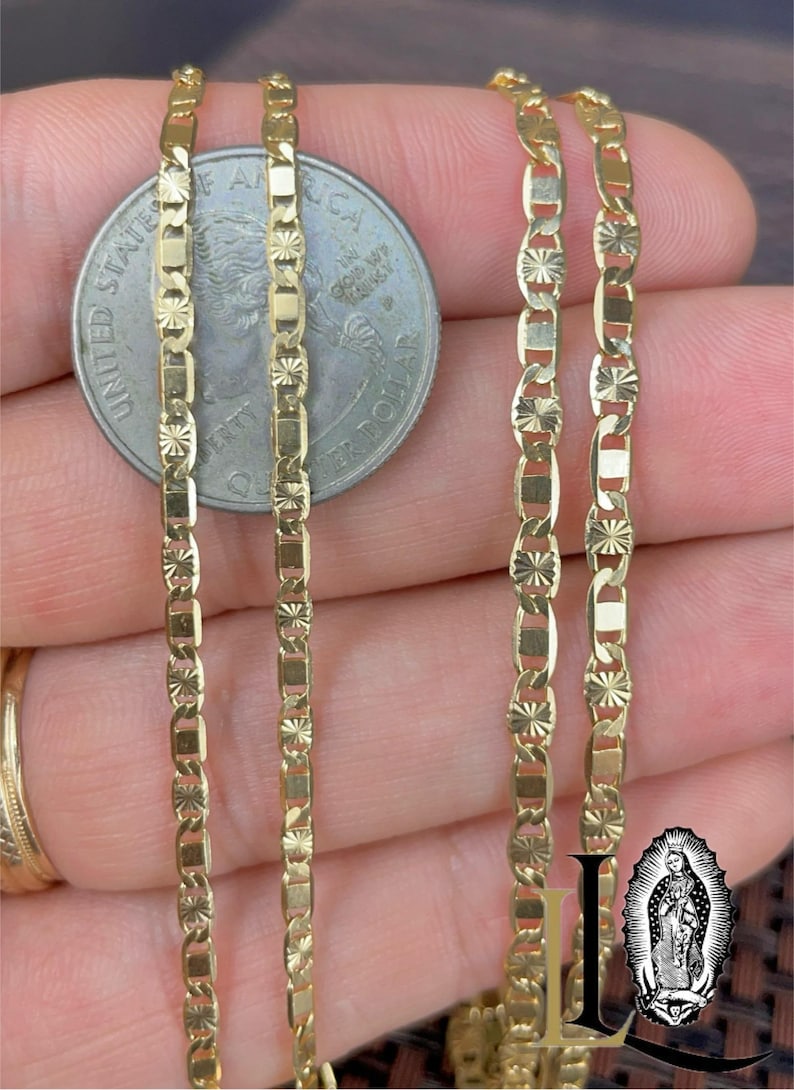 May include: Close-up of several gold-colored chain necklaces with intricate geometric designs. A US quarter coin is placed in the center for size comparison. The chains have a bright, reflective finish, suggesting they are made of a precious metal.