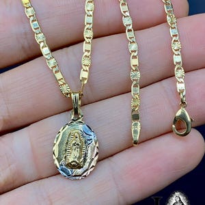 May include: A gold chain necklace with a pendant featuring a depiction of the Virgin Mary. The chain is a Figaro style with alternating links. The pendant is oval shaped and has a detailed design.