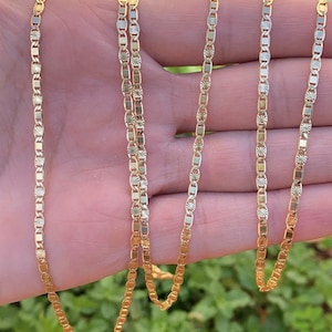May include: A gold chain necklace with a delicate, patterned design. The chain is made of multiple strands and is shown draped over a hand.