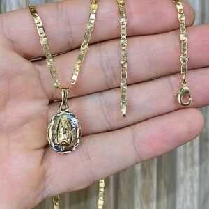 May include: A gold chain necklace with a pendant featuring a detailed image of the Virgin Mary. The chain is a delicate, patterned design.