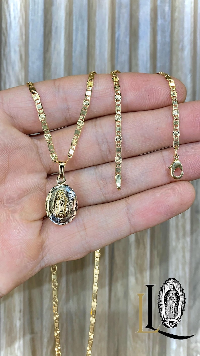 May include: A gold chain necklace with a pendant featuring a detailed image of the Virgin Mary. The chain is a delicate, patterned design.