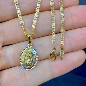 May include: A gold chain necklace with a pendant featuring a detailed image of the Virgin Mary. The chain is a delicate, patterned design.