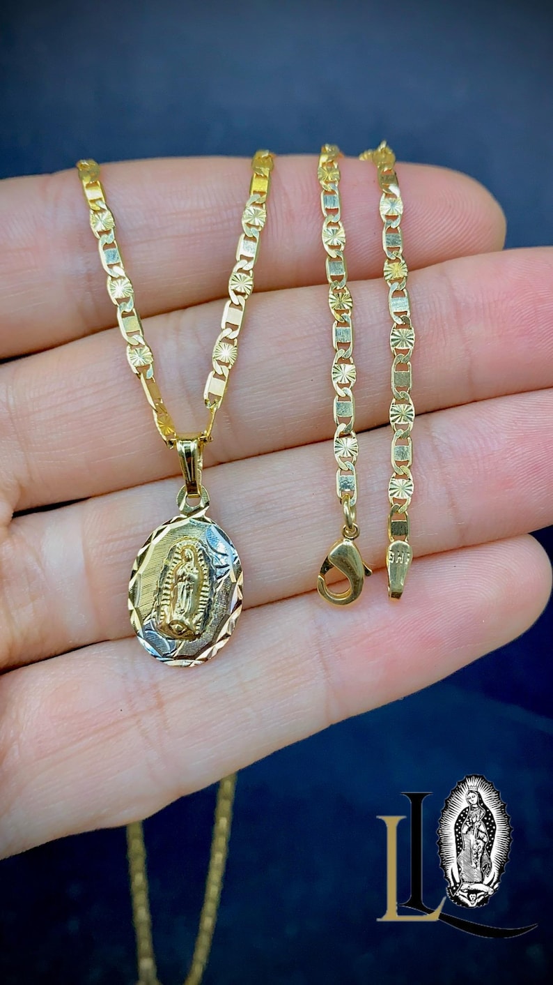 May include: A gold chain necklace with a pendant featuring a detailed image of the Virgin Mary. The chain is a delicate, patterned design.