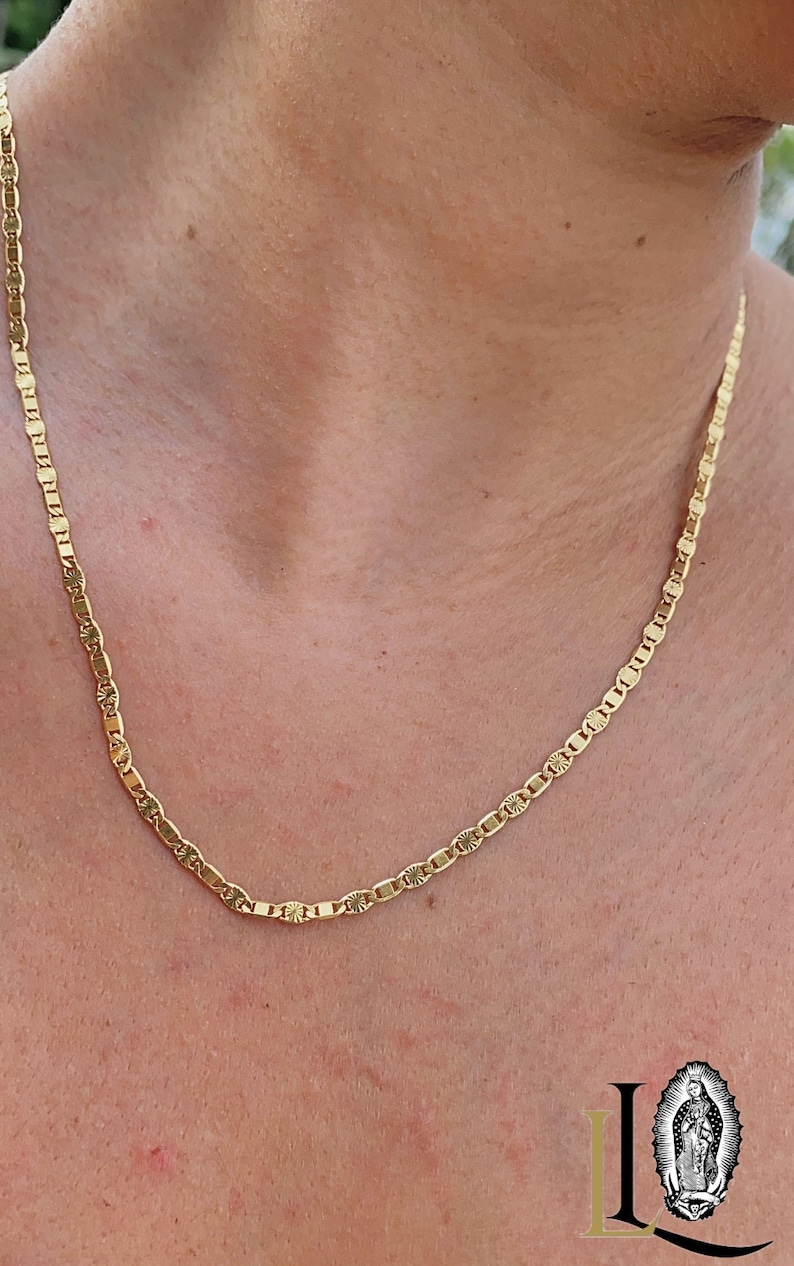 May include: A gold chain necklace with a delicate, patterned design. The chain is made of small, oval-shaped links.