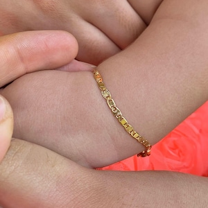 May include: A gold chain bracelet with a delicate design. The bracelet is worn on a child's wrist.
