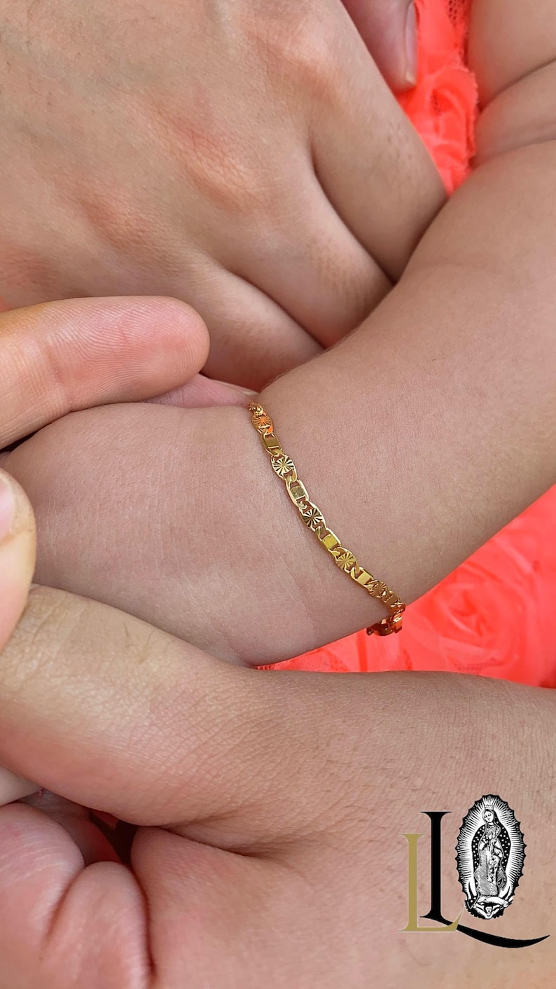 May include: A gold chain bracelet with a delicate design. The bracelet is worn on a child's wrist.