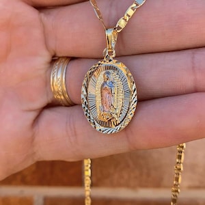 May include: A gold chain necklace with a detailed oval pendant featuring a depiction of the Virgin Mary. The pendant is two-toned, with a gold and rose gold finish.