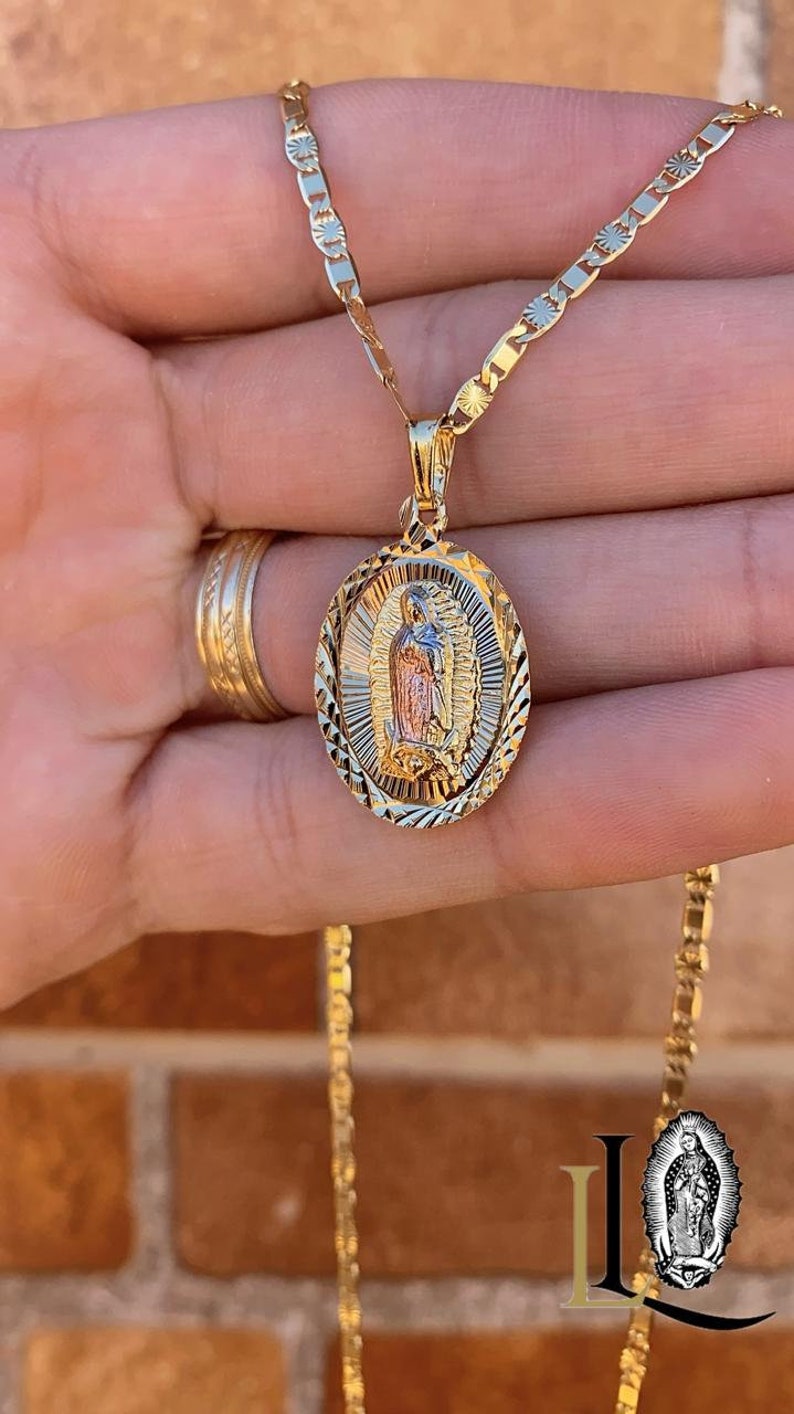 May include: A gold chain necklace with a detailed oval pendant featuring a depiction of the Virgin Mary. The pendant is two-toned, with a gold and rose gold finish.