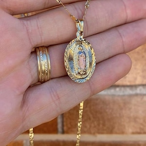 May include: A gold chain necklace with a pendant featuring a detailed image of the Virgin Mary. The pendant is oval-shaped and has a textured design.