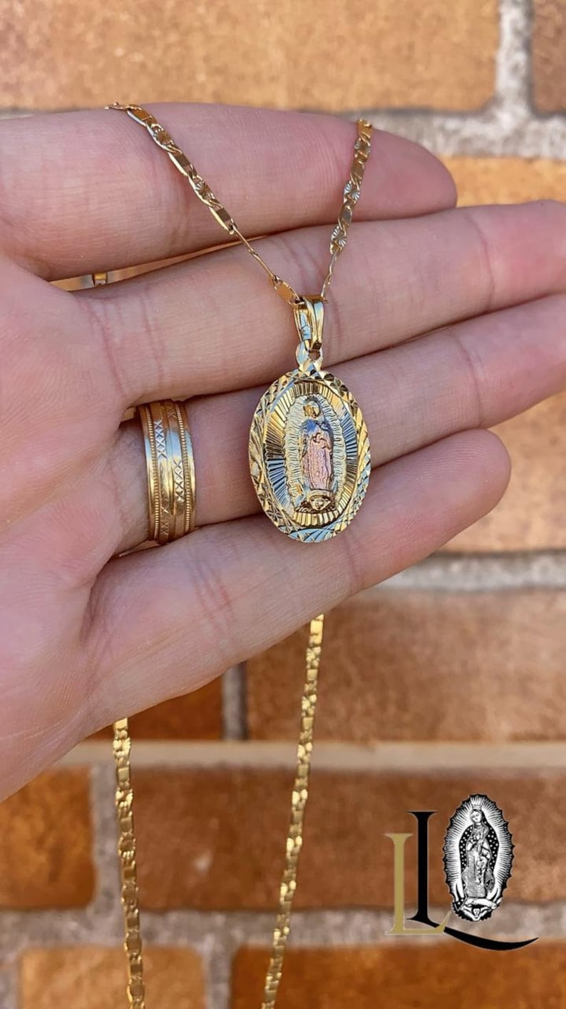 May include: A gold chain necklace with a pendant featuring a detailed image of the Virgin Mary. The pendant is oval-shaped and has a textured design.
