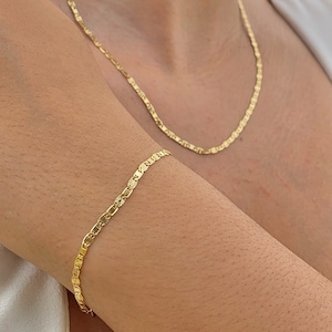 May include: A gold chain necklace and bracelet with a delicate, patterned design. The necklace is worn around the neck and the bracelet is worn on the wrist.