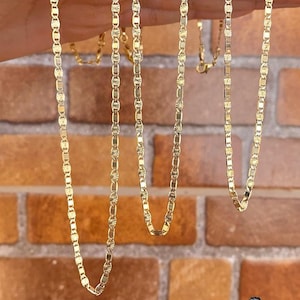 May include: Four gold chains with a diamond-shaped pattern on each link. The chains are hanging from a hand.