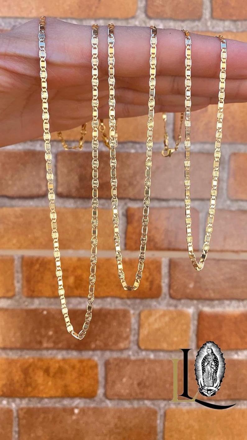 May include: Four gold chains with a diamond-shaped pattern on each link. The chains are hanging from a hand.