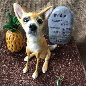 May include: A ceramic figurine of a tan chihuahua dog with a tombstone that reads "Pi&ntilde;a Feared By All - Loathed By Many Tolerated By Most Loved By Few Besos Munifica RIP".