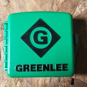 Op de afbeelding: Een felgroene, vierkante gereedschapskist met de merknaam "GREENLEE" in het wit. Het heeft een zwarte ruit met een witte "G". De kist heeft een scharnierzijde en een sluiting.