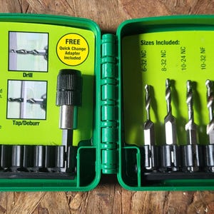 May include: Open green plastic drill bit set. The case displays various drill bit sizes for metal and plastic. The set includes a quick change adapter. The text on the case indicates the drill bits are for steel, copper, brass, aluminum, and plastic.