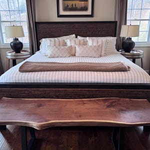 Può includere: Una camera da letto con un letto in legno e una panca con bordo vivo. Il letto ha una trapunta a righe e cuscini decorativi. Due lampade sono sui comodini. La stanza ha grandi finestre e tende marroni.