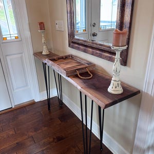 Può includere: Un tavolo consolle in legno con un piano in legno vivo e gambe a forcina nere. Il tavolo è decorato con due candelabri e un vassoio in legno.