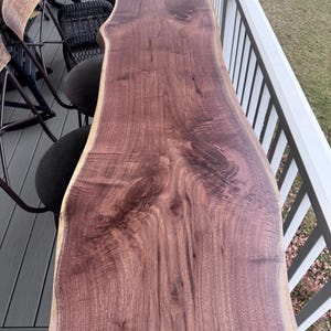 Puede incluir: Una mesa de madera con borde natural, de un rico tono marrón rojizo. La superficie de la mesa muestra la veta natural y la forma única de la madera. La mesa mide aproximadamente 244 cm de largo.