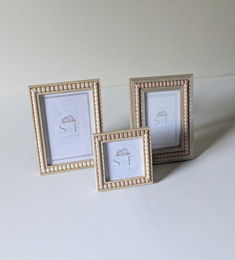 May include: Three picture frames with light wood finishes and beaded detailing along the inner edges. Each frame contains a white insert featuring the text S&F and a small house illustration. The set includes two rectangular frames and one square frame.