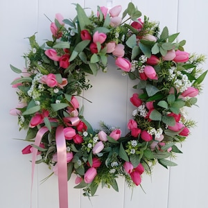 May include: A pink and green floral wreath with a pink ribbon. The wreath is made of artificial tulips and greenery.