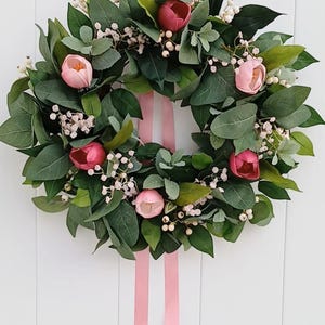 May include: A green wreath with pink flowers and white berries, decorated with a pink ribbon.