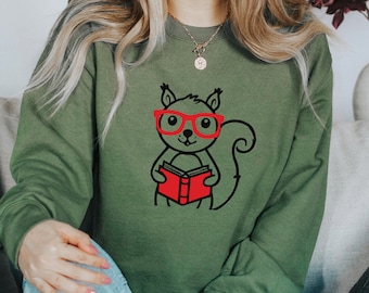 May include: A green sweatshirt with a graphic of a squirrel wearing red glasses and holding a red book.