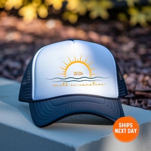 May include: A trucker hat with a white front panel and a navy blue brim and mesh back. The front features a yellow sun graphic with the year 2026 and the words "smith on vacation" in a script font. The hat is designed for vacation.