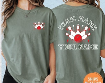 May include: An olive green t-shirt featuring a small graphic on the front left chest of white bowling pins and a red bowling ball. The back of the shirt displays the same bowling graphic with the text TEAM NAME and YOUR NAME in white.