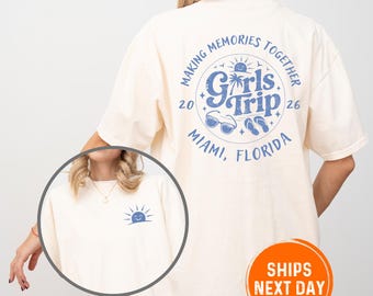 May include: Cream-colored t-shirt with a blue graphic on the back that reads "Making Memories Together Girls Trip 26 Miami, Florida." A smaller sun graphic is on the front. The shirt is a relaxed fit.