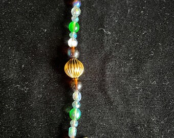 May include: A gold and brown beaded charm with a star-shaped pendant. The beads are iridescent and have a variety of colors, including green, blue, and brown.