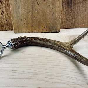 May include: A bottle opener made from a brown antler with a silver metal opener. The antler is polished and has a natural, rustic look.